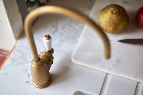 Aged brass instant hot water tap with white lever handle on marble countertop