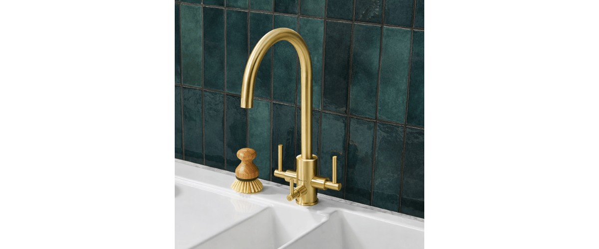 brushed brass three way tap installed on a white sink with green tiles in the background