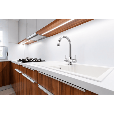 A modern kitchen sink setup featuring a goose neck chrome faucet mounted on a white countertop with a matching white basin, set against white cabinetry and wood-grain lower cabinets.