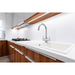 A modern kitchen sink setup featuring a goose neck chrome faucet mounted on a white countertop with a matching white basin, set against white cabinetry and wood-grain lower cabinets.