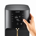 A close-up of a black ecosoft water dispenser with a digital display screen and a hand touching the touch panel, set against a clean white background.