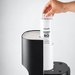 A hand is shown removing a white Ecosoft RO reverse osmosis water filter cartridge from a black and white water dispenser against a light gray background.