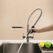 Person using a modern pull down spray on a kitchen faucet with a beige wall background