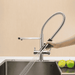 Modern kitchen faucet with a hand washing a dish under running water, against a beige wall with a lemon and apple