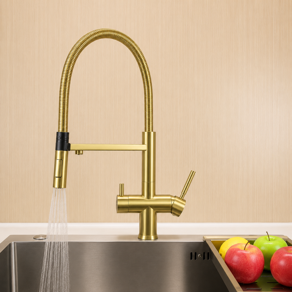 brushed brass kitchen faucet with water flowing into a sink, against a beige wall with apples and lemon