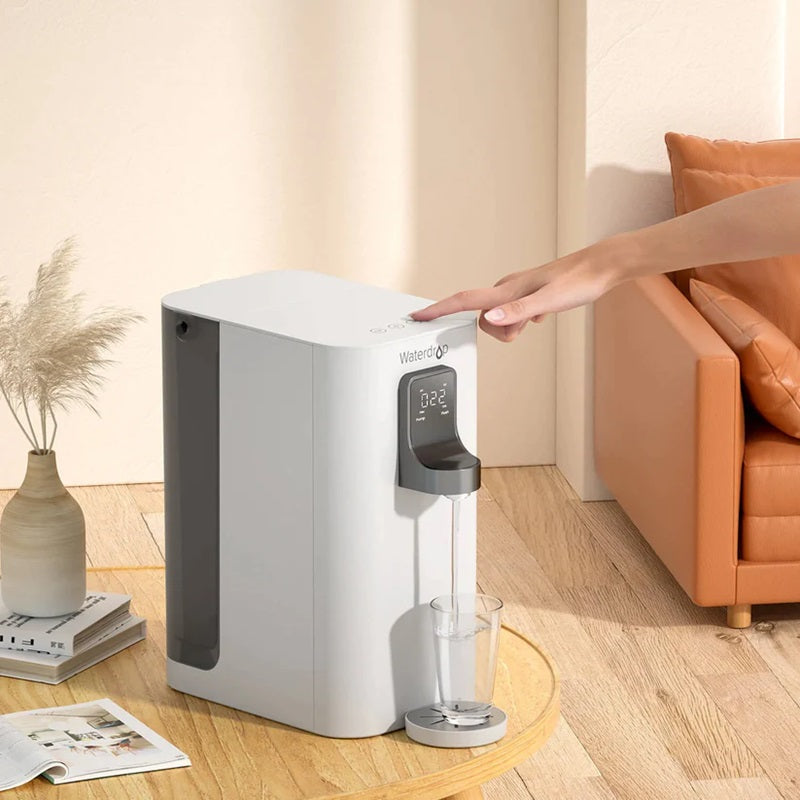 A countertop dispenser pouring water in the living room with a sofa in the background